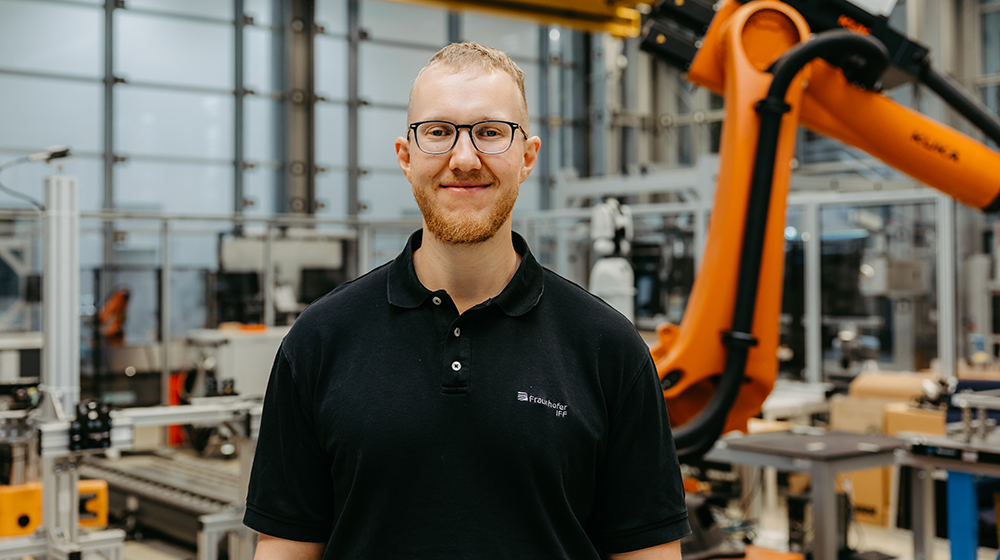 Junior Professor Sebastian Lang stands in front of an industrial machine in a workshop (c) Jana Dünnhaupt University of Magdeburg