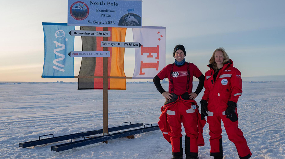 Prof. Thomas Richter and Dr. Carolin Mehlmann stand on the ice at the North Pole in front of various flags (Photo: Alfred Wegener Institute / Esther Horvath)